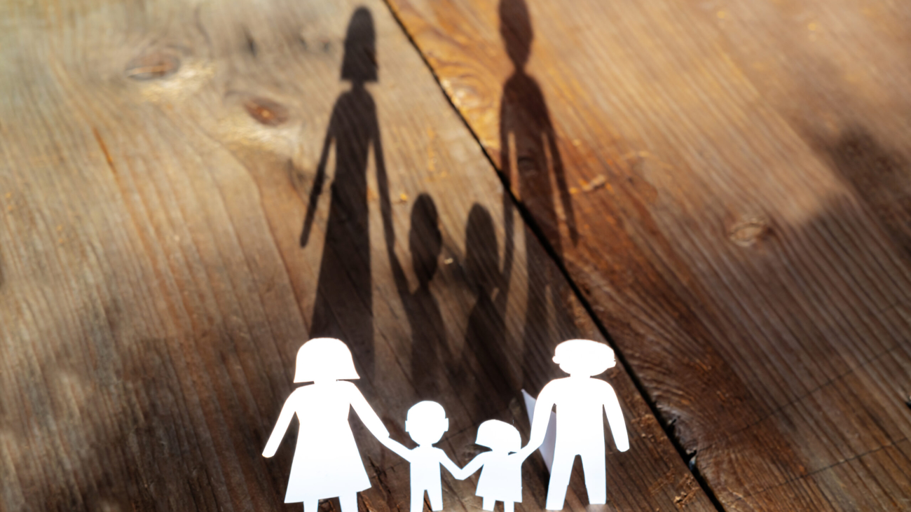 The family of paper cut placed on a wooden table. There is a shadow of a family holding hands, an impressive and warm image concept