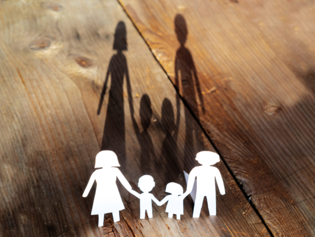 The family of paper cut placed on a wooden table. There is a shadow of a family holding hands, an impressive and warm image concept